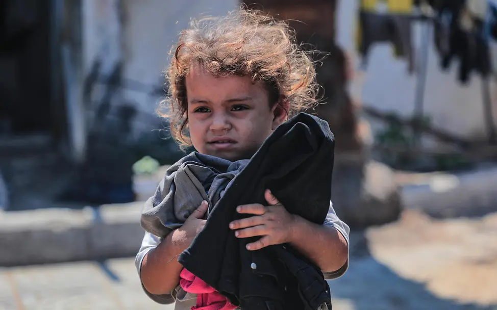 Gaza Waffenruhe: Ein Kleinkind in einem Flüchtlingscamp hält Kleidung im Arm. 