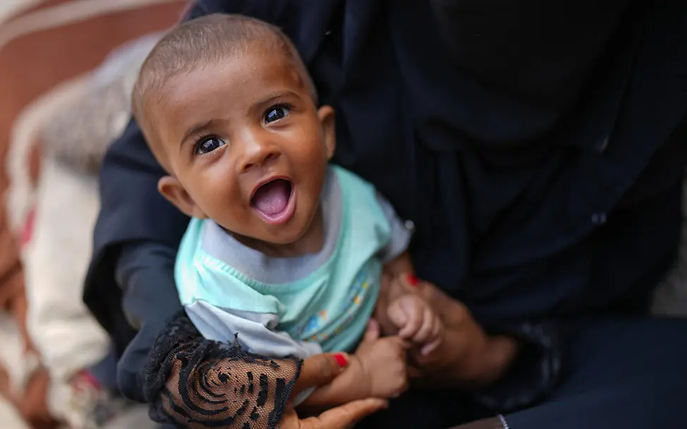 Jemen: Baby lacht im Schoß der Mutter.