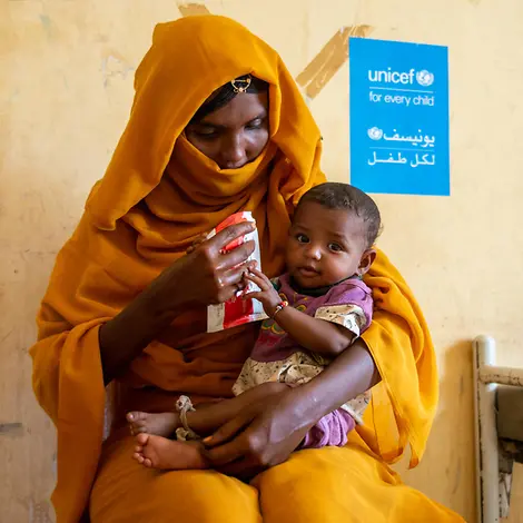 EIne Mutter mit ihrem Kind im Sudan | © UNICEF/UNI707416/Rajab Eine Mutter hat ihr Kind auf dem Schoß und gibt ihm therapeutische Zusatznahrung