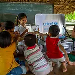 Eine Gruppe Kinder sitzen um eine Lehrerin herum, die mit einem Kindergarten in der Kiste lernen spielerisch und einfach macht.