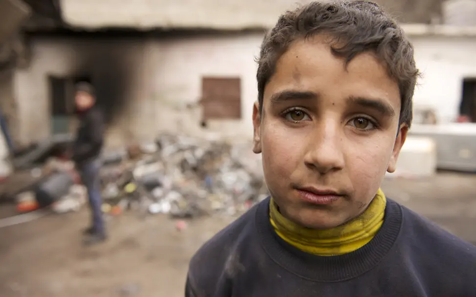 Der 14-jährige Ahmed steht vor der Recycling-Anlage. Sein Blick zeigt wie anstrengend die Arbeit für ihn ist.