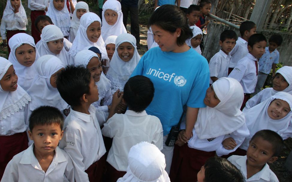 Indonesien: UNICEF-Mitarbeiterin steht gemeinsam mit Schülern vor einer Schule.